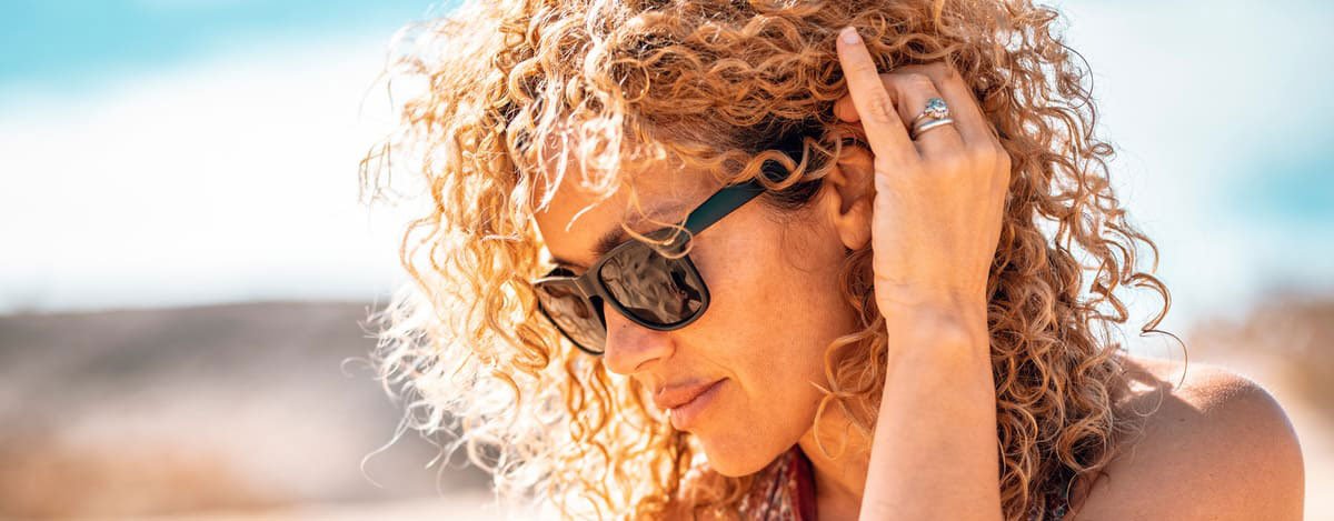 Imagem de uma mulher com óculos de sol e cabelo encaracolado.