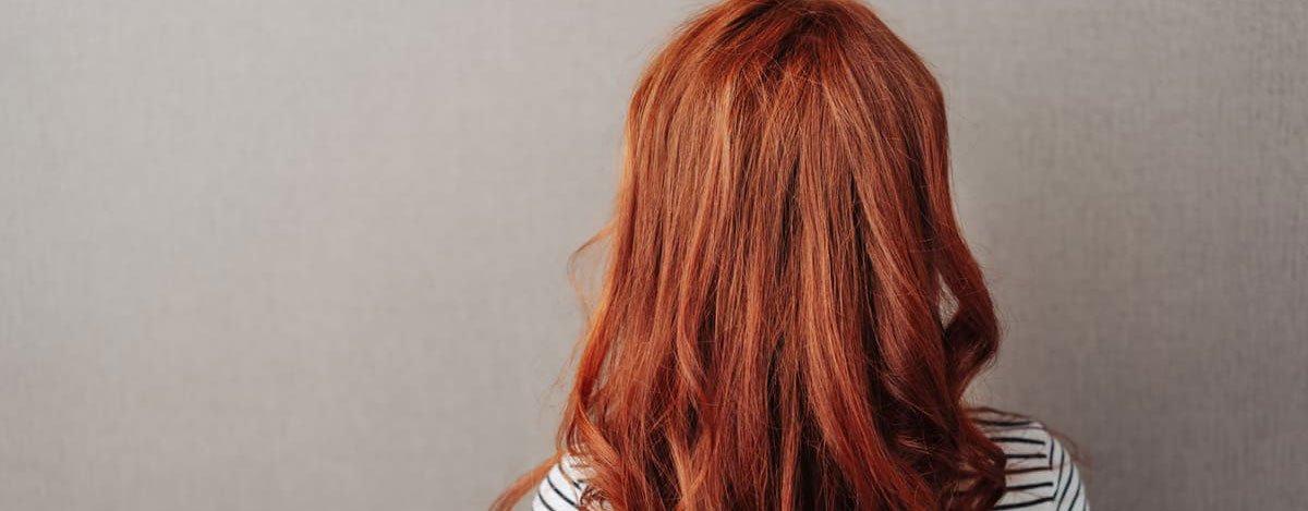 Imagem de uma mulher de cabelo ruivo, vista de costas.