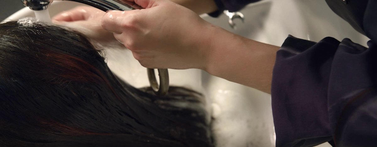 O foco está numa mulher a lavar o cabelo num salão, ilustrando o programa de saúde mental da L’Oréal para profissionais da área.