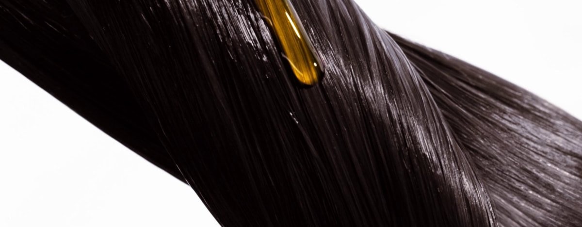 Aplicação passo a passo de óleo capilar para reparar o cabelo seco e danificado, mostrando pequenas quantidades aquecidas nas mãos e depois aplicadas uniformemente ao longo do comprimento e nas pontas.