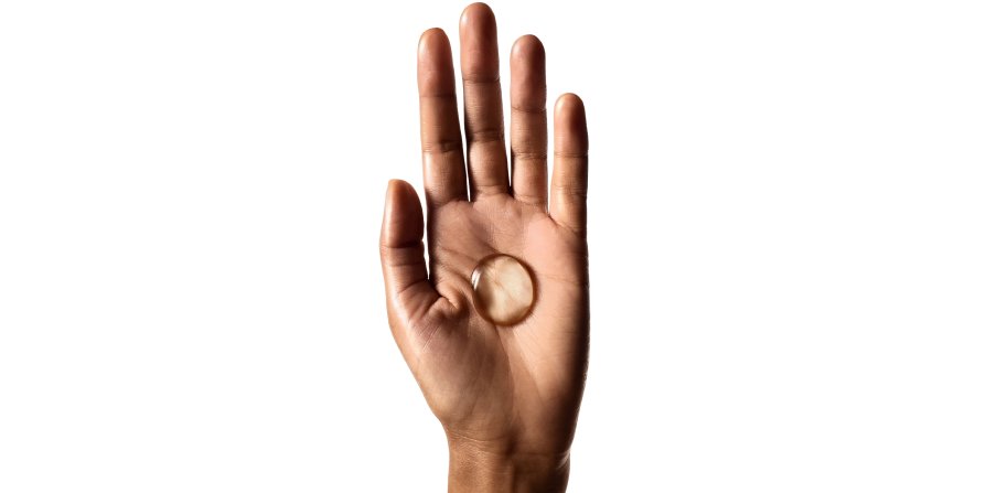 Observe uma mão a segurar uma gota de champô, ilustrando que a utilização da quantidade e do método de aplicação corretos ajuda a reduzir a oleosidade do cabelo.