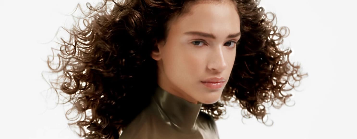 Mulher a posar e a exibir os seus cabelos encaracolados saudáveis, radiantes e bem definidos, com movimento, definição e brilho natural.