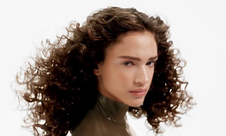 Mulher a posar e a exibir os seus cabelos encaracolados saudáveis, radiantes e bem definidos, com movimento, definição e brilho natural.