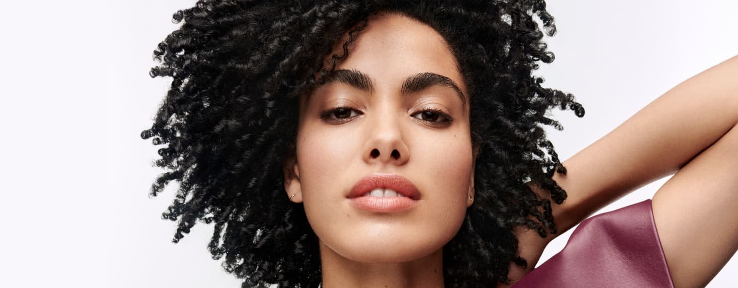 Mulher a posar e a exibir os seus cabelos escuros e encaracolados bem definidos, com um aspeto saudável, movimento e textura natural realçada.