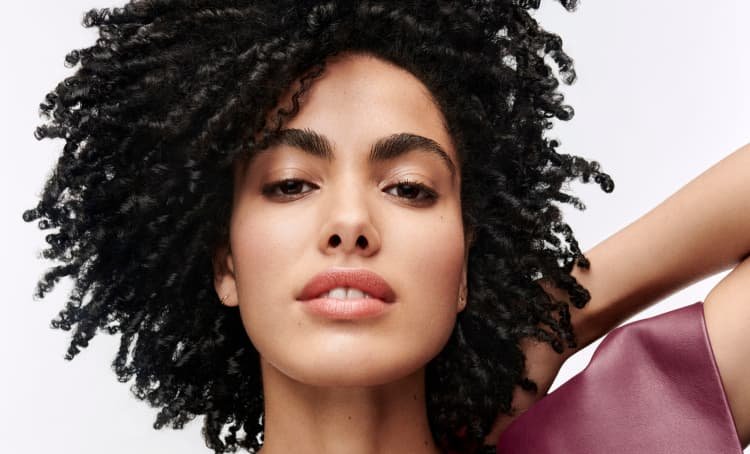 Mulher a posar e a exibir os seus cabelos escuros e encaracolados bem definidos, com um aspeto saudável, movimento e textura natural realçada.
