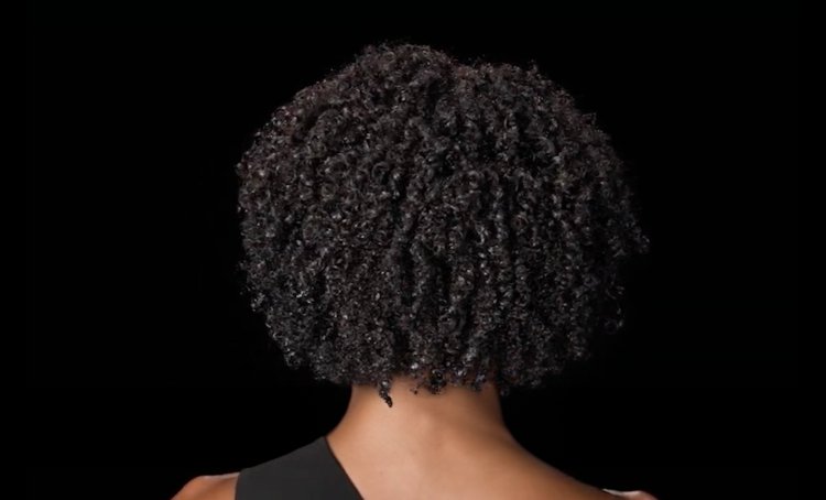 Mulher vista de costas com cabelo encaracolado, brilhante e saudável, ilustrando dicas e técnicas para desembaraçar os caracóis sem causar danos.